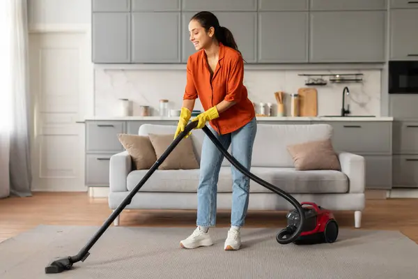 Cheerful Young Woman Orange Shirt Jeans Using Vacuum Cleaner Rug — Stock Photo, Image