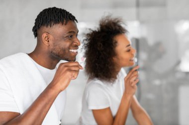 Romantik siyah eşlerin diş bakımı rutinlerini, ev banyosunun iç tarafındaki aynanın yanında dişlerini fırçalarken yan görüntüler.