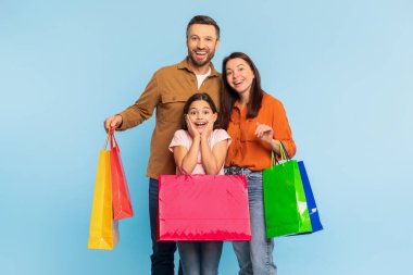 Heyecanlı üç kişilik aile, mavi arka planda renkli alışveriş torbaları bulundurarak sezonluk satışlara ve indirimlere hazır hale geldiler. Neşeli müşteriler Kara Cuma teklifini kutluyor.