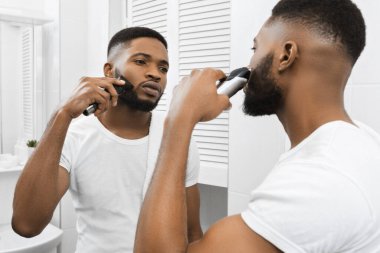 Afro adam banyoda aynaya bakarak yüzünü tıraş ediyor.