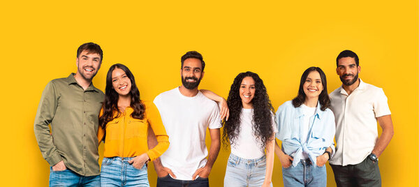 Five cheerful friends students with casual outfits smiling and standing close together, showcasing diversity and unity on a mustard yellow backdrop, panorama, studio. Study, education