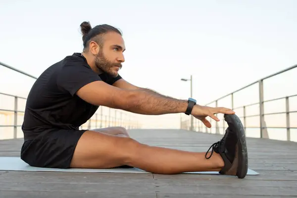 身穿黑色运动服的年轻人在外面进行健身锻炼时伸长着脚趾头 瑜伽和健康的生活方式的概念 运动员提高灵活性的侧面观点 — 图库照片
