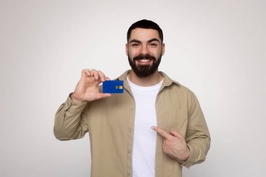 Haki gömlekli ve beyaz tişörtlü neşeli sakallı Arap adam mavi bir kredi kartı gösterip diğer eliyle işaret ederek iyi bir anlaşma ya da finansal seçim öneriyor.