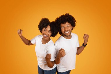 Binlerce yıllık Afro-Amerikan çifti yumruklarını sıkarken, portakal rengi stüdyo arka planında el kaldırırken, kameraya gülümserken, sonuçtan mutlu bir şekilde.