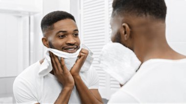 Afro adam tıraş tan sonra yüzünü kurutuyor, banyoda aynaya bakıyor. Mans günlük bakım konsepti