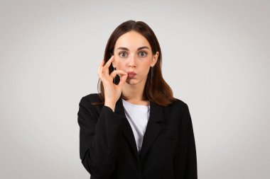 Siyah takım elbiseli oyuncu beyaz iş kadını parmaklarıyla küçük bir miktar hareket ederken komik surat yapıyor, profesyonel bir ortamda neşeli bir tarafı var.