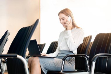 Boş konferans odasında çalışan, telefonla konuşan ve dizüstü bilgisayar kullanan kendine güvenen bir kadın.