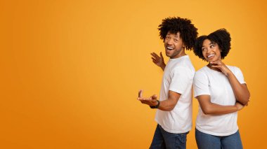 Bin yıllık Afro-Amerikan çifti turuncu stüdyo arka planında poz veriyor, kadın ve erkek arka arkaya kameraya bakıyor, boş fotokopi alanı modeli, web-afişi