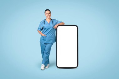 Kendine güvenen hemşire, tıbbi uygulama tanıtımı için geniş, boş bir akıllı telefon modeline yaslanıyor, steteskopla önlük giymiş, mavi arka planda.