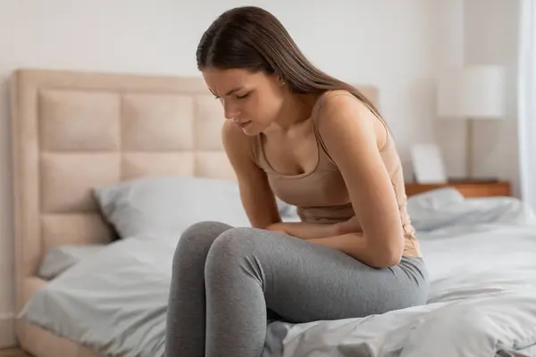 Gündelik Giyinen Genç Bir Kadın Elleri Karnında Yatağında Oturuyor Rahatsızlık — Stok fotoğraf