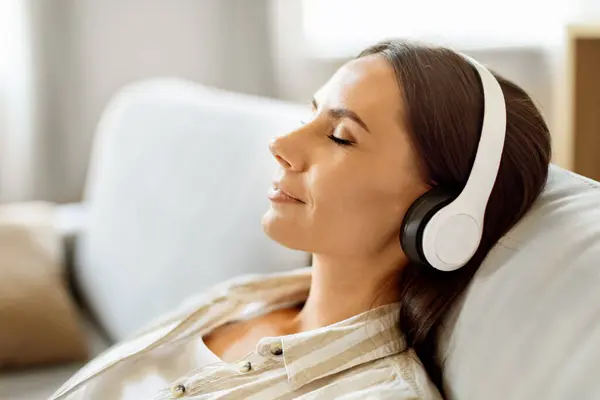 Mujer Joven Pacífica Sentada Sofá Escuchando Música Través Sus Auriculares —  Fotos de Stock
