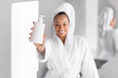 Bornozlu Afro-Amerikan Kadın, Cilt Bakımı İçin Kozmetik Şişesi Gösteriyor, Modern Tuvalette Duruyor. Sığ Derinlik, Seçici Odaklanma Güzellik Ürünleri