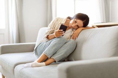 Onun aramasını bekliyorum. Evde koltukta otururken Akıllı Telefona Bakan Üzgün Genç Kadın, Depresyondaki Avrupalı Kadın Cep Telefonu, SMS veya İnternet Haberleri Okuma, Kopyalama Alanı