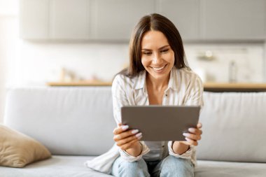 Modern Teknolojiler. Gülümseyen Genç Kadın Evinde Dijital Tablet Kullanıyor, Mutlu Güzel Kadın İnternet Tarıyor ya da İnternetten Alışveriş Yapıyor, Sıcak Oturma Odasında Oturuyor, Boşluğu Kopyala