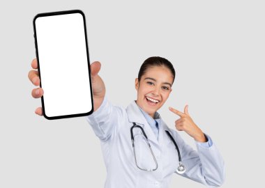 Kafkasyalı genç bir doktor, sağlık uygulaması ekranı için boş bir akıllı telefon ekranı sunuyor, stetoskopla, dijital sağlık promosyonu için ideal. Sağlık uygulaması, blog, dikkat