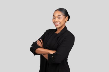 Kendine güvenen Afro-Amerikan iş kadını büyüleyici bir gülümseme ile kolları çapraz duran klasik bir siyah spor ceket içinde liderlik ve profesyonellik yayıyor.