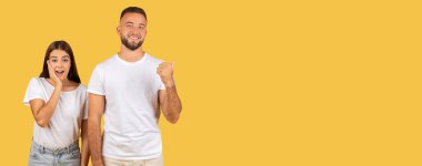 Sade beyaz t-shirtler ve kot pantolon giyen iki neşeli genç kadın şaşırmış, adam da başparmağını kaldırıyor.