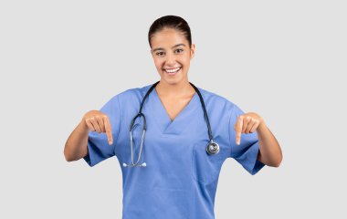 Mavi önlüklü neşeli Avrupalı doktor güvenli bir şekilde boş bir yeri işaret ediyor, sağlık hizmetleri terfileri veya bilgilendirme içeriği için mükemmel.