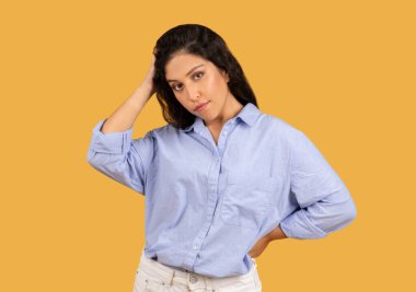 Kendine güvenen, koyu renk saçlı, sıradan mavi gömlekli genç bir kadın turuncu arka planda, stüdyoda düşünceli bir şekilde poz veriyor. Seç, moda yaşam tarzı, iş, reklam ve teklif