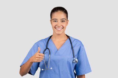 Mavi önlüklü Avrupalı kadın doktor, güvenilirliği ve sağlık deneyimini özetliyor, sağlık hizmetlerini onaylıyor, tavsiye ediyor.