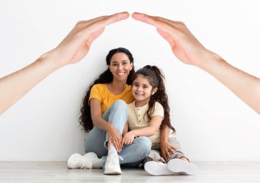 Ortadoğulu güzel bir anne ve küçük kız yeni dairede, kolajda, beyaz duvarın üstünde, ellerin altında oturuyorlar. Bekar annelik, ebeveynlik.