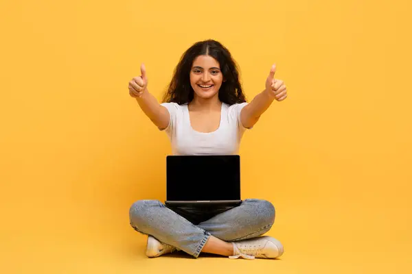 素晴らしい教育ウェブサイト コース オンライン学習 陽気で魅力的なカーリーの若いヒンドゥーの女性は空のスクリーンが付いているコンピュータと床に座って 親指のアップを示し 黄色いスタジオの背景 — ストック写真