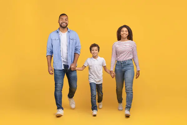 3人の手を握り 黄色い背景を歩いている黒人の家族 若いアフリカ系アメリカ人の両親と リラックスして幸せなライフスタイル コピースペースを体現したカジュアルな服に息子 — ストック写真