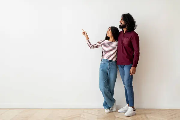 愛するミレニアムヒンドゥー教のカップル幸せな男性と女性は 空の家で白い空白の壁の背景の上にコピースペースを指し 広告を示しています モーゲージ — ストック写真