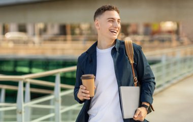 Köprüde yürüyen neşeli genç bir adam, elinde bir kahve fincanı ve dizüstü bilgisayarla, beyaz bir gömleğin üzerine denizci ceketi giymiş, omzunda bir kurye çantası, başka tarafa bakıyor ve gülüyor.