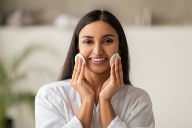 Neşeli, güzel, esmer, uzun saçlı, bin yıllık kızılderili kadın bornoz giyip asit pedleriyle yüzünü temizliyor. Çekici kadın makyaj malzemelerini çıkarıyor, banyoda pamuk pedleri ve losyon kullanıyor.