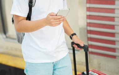 Çantalı, sırt çantalı, pasaportlu ve biletli bir adam telefonda yazıyor, sohbet ediyor, tren istasyonunda veya havaalanında ulaşımı bekliyor. Kapatın. Teknoloji, uygulama, seyahat