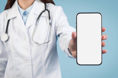 Beyaz laboratuvar önlüklü bir tıp uzmanı mavi arka planda tele-sağlık potansiyelini vurgulayan boş akıllı telefon ekranı sunuyor.