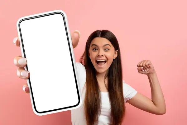 在线报价 欣喜若狂的少女庆祝胜利 挥动拳头 在镜头前展示白色空白屏幕的大手机 站在粉色背景下感情用事 复制空间 — 图库照片