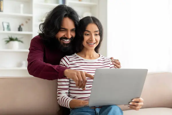 网上教育 远程工作和购物 一对快乐的印度夫妇 一边看笔记本电脑 一边选购或看电视课 坐在客厅的沙发上 一边抄袭空间 — 图库照片