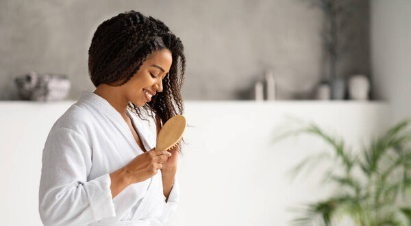 Beautiful African American Woman Combing Her Hair With Bamboo Brush At Home, Attractive Black Female Standing In Bathroom Interior, Making Morning Beauty Routine At Home, Copy Space