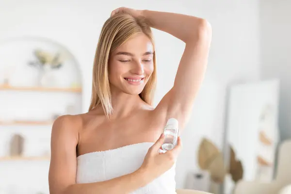 漂亮的金发女人在腋下涂上滚动式止汗剂 专注于现代浴室的卫生和新鲜感 使用除臭剂防止汗水和气味 — 图库照片