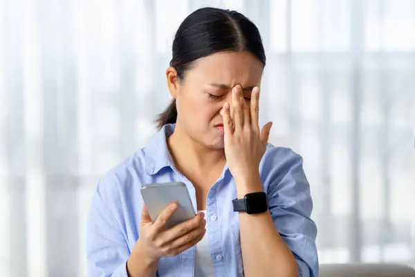 スマートフォンが額に触れる不幸なアジアの女性のクローズアップ 悪いニュースをオンラインで読んだり 否定的な電子メールを受け取った メッセージ 悲しみを感じる 泣いている 家庭のインテリア コピースペース — ストック写真