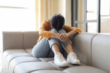 Üzgün Hintli kadın, başı aşağıda ve kolları dizlerine dolanmış bir şekilde koltukta oturuyor. Depresyondaki genç kadın, hüzün ya da hayal kırıklığı, acı çeken hayat sorunları, boş alan.