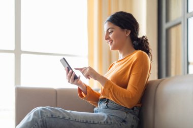 Çevrimiçi sipariş. Mutlu Hintli Kadın Evde Akıllı Telefon Kullanıyor, İnternette Milenyum Doğulu Kadın Satın Alma Gülümsüyor, Cep Telefonunda Yeni Uygulama Bakıyor ya da Sosyal Ağ Kaydırıyor, Kopyalama Ağı