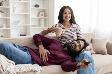 Neşeli genç Hintli aşıklar evde eğleniyor, TV 'de film ya da şov izliyor, kanepede iç tarafta oturuyor, kahve içiyor, birlikte mutlu bir hafta sonu geçiriyor, boş bir alanda mutlu bir çift.