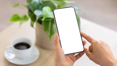 Mobil uygulama ya da internet reklamı için beyaz ekran kopyalama alanı olan tanımlanamayan bir bayan telefon tutuyor. Evde dinlenen, kahve içen, akıllı telefon kullanan bir kadın.