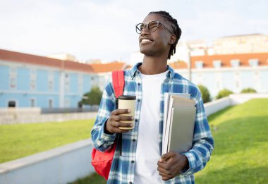 - Öğrencilik. Sıradan siyah bir adam elinde bir dizüstü bilgisayar ve bir fincan kahve, dersten sonra gülümseyen çalışmanın tadını çıkaran, açık hava üniversitesindeki modern akademik yaşam tarzını somutlaştıran