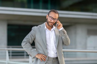 Takım elbiseli ciddi bir iş adamı açık havada telefonla konuşuyor, kendine güvenen bir girişimci el ele tutuşuyor, şehir planına karşı duruyor, aktif iş iletişimini resmediyor.