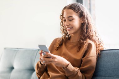 Avrupalı ergen kız internette internette geziniyor, çevrimiçi iletişim ve uygulama kullanımına katılıyor, kaygısız ve rahat evinde mutlu bir şekilde oturuyor. Mobil uygulamalar, aygıtlar