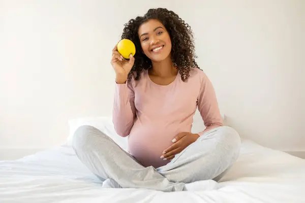 健康的なスナック 自宅でベッドでリラックスしながらオーガニックリンゴを保持している黒人妊婦と優しく腹に触れる 幸せなアフリカ系アメリカ人期待女性はビタミン食品を楽しんで スペースをコピーします — ストック写真