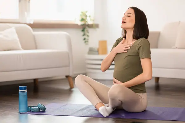 怀孕的欧洲裔女士在怀孕期间进行冥想和呼吸运动以放松身心 在家里坐在瑜伽垫上 双手放在胸部和腹部 空旷的空间 — 图库照片