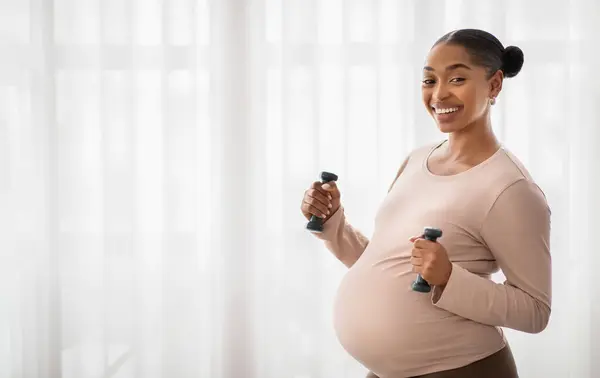 笑顔の妊娠中の黒人女性は バーベルで運動し カメラを見て笑顔 コピースペース付きのパノラマ アフリカ系アメリカ人は ダンベルを使って家庭で女性のトレーニングを期待しています 妊娠中のスポーツ — ストック写真
