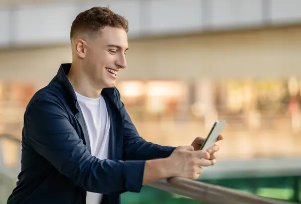 Een Glimlachende Blanke Jongeman Met Smartphone Leunend Leuning Gekleed Een — Stockfoto