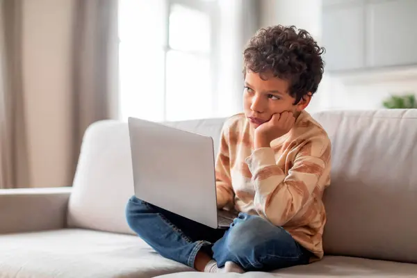 Pensiv Liten Svart Pojke Sitter Med Laptop Soffan Och Tittar — Stockfoto