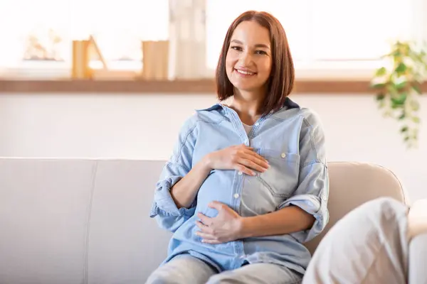 Европейская Беременная Женщина Излучающая Счастье Сидит Диване Комфортом Нежно Прикасаясь — стоковое фото